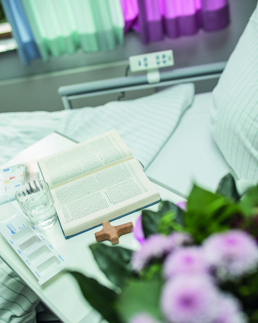 Krankenbett mit Blumen und Bibel